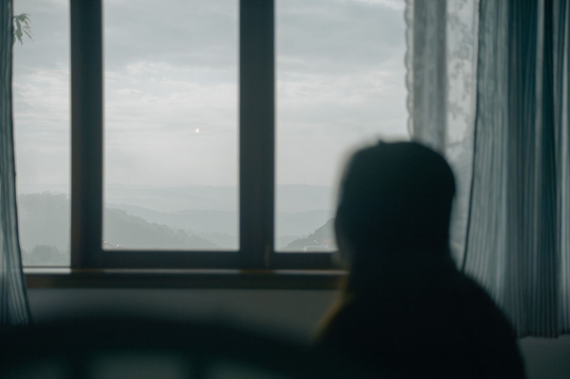 Une silhouette à la fenêtre, regardant un paysage calme au petit matin
